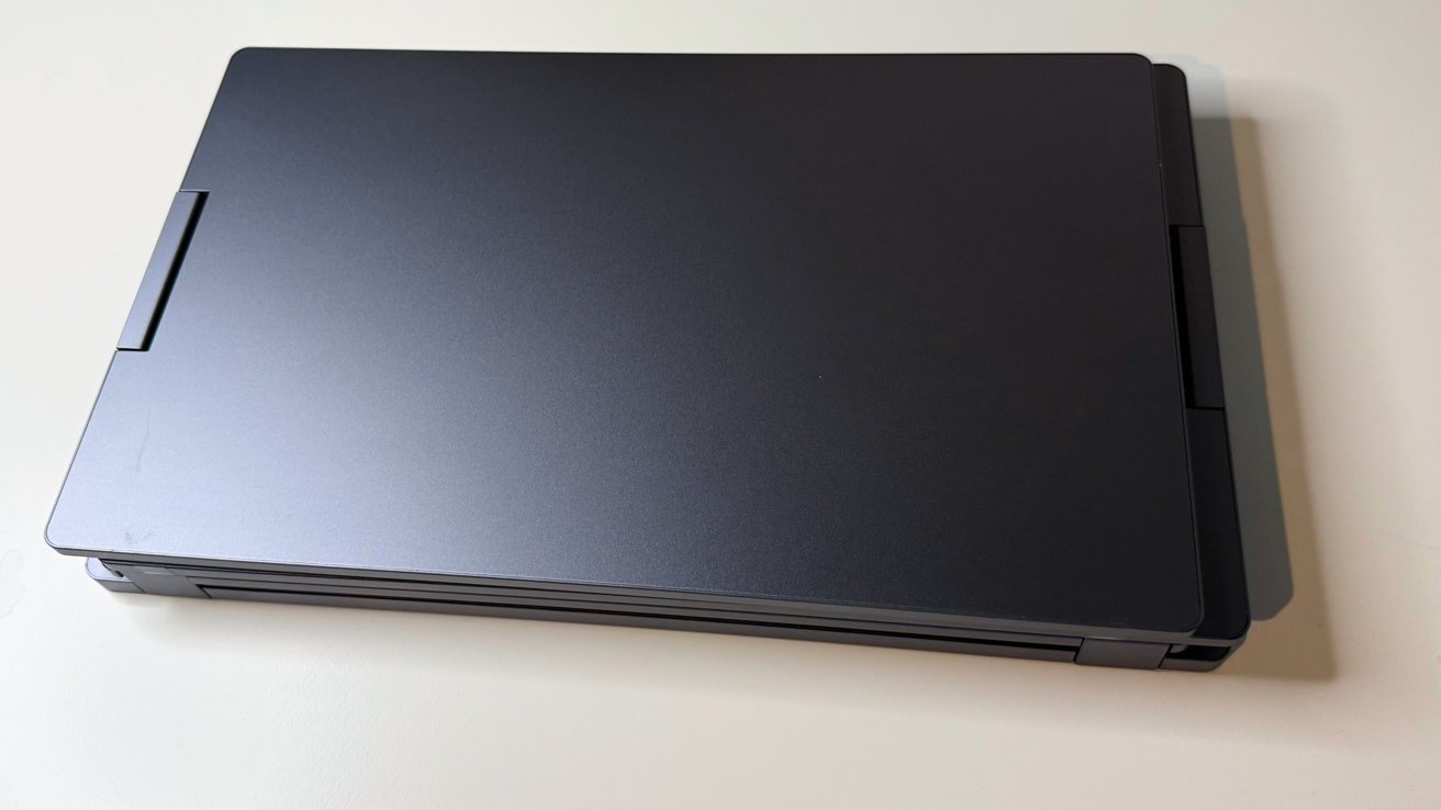 Closed black laptop on a light surface, viewed from above, showing its matte finish and hinges.