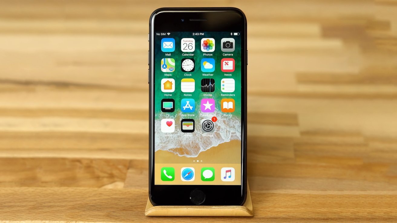 Smartphone with app icons displayed, including Mail, Calendar, Photos, and Music, placed on a wooden stand in front of a wooden background.