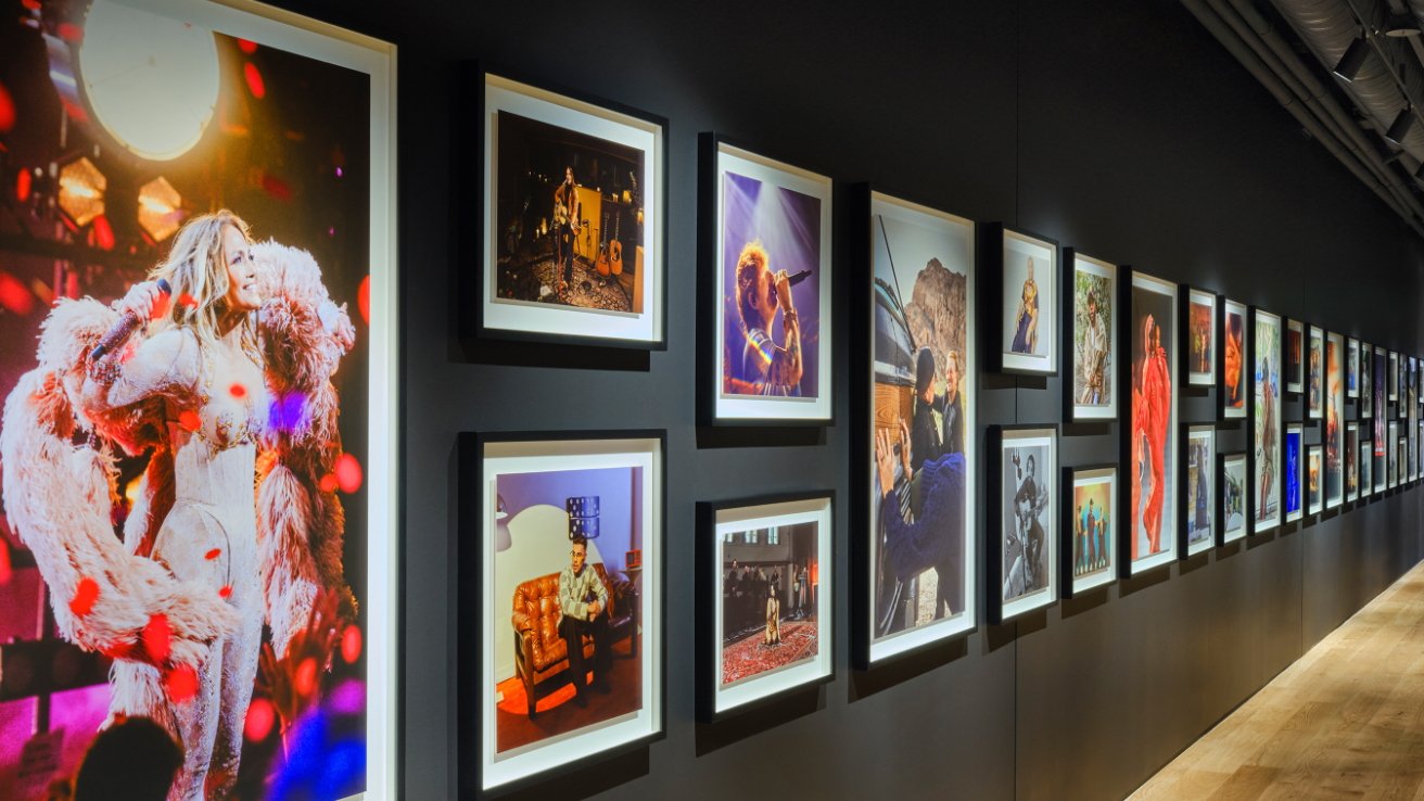 A gallery wall displaying various framed photographs, predominantly featuring musicians performing and candid moments captured in vibrant colors, under dim warm lighting.