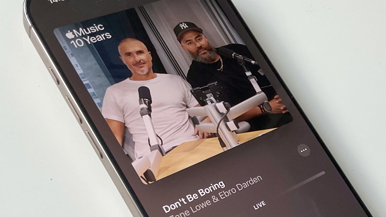 Two men sit at a podcast desk with microphones. The Apple Music 10 Years logo appears in the corner and 'Don't Be Boring' text is visible on a phone screen.