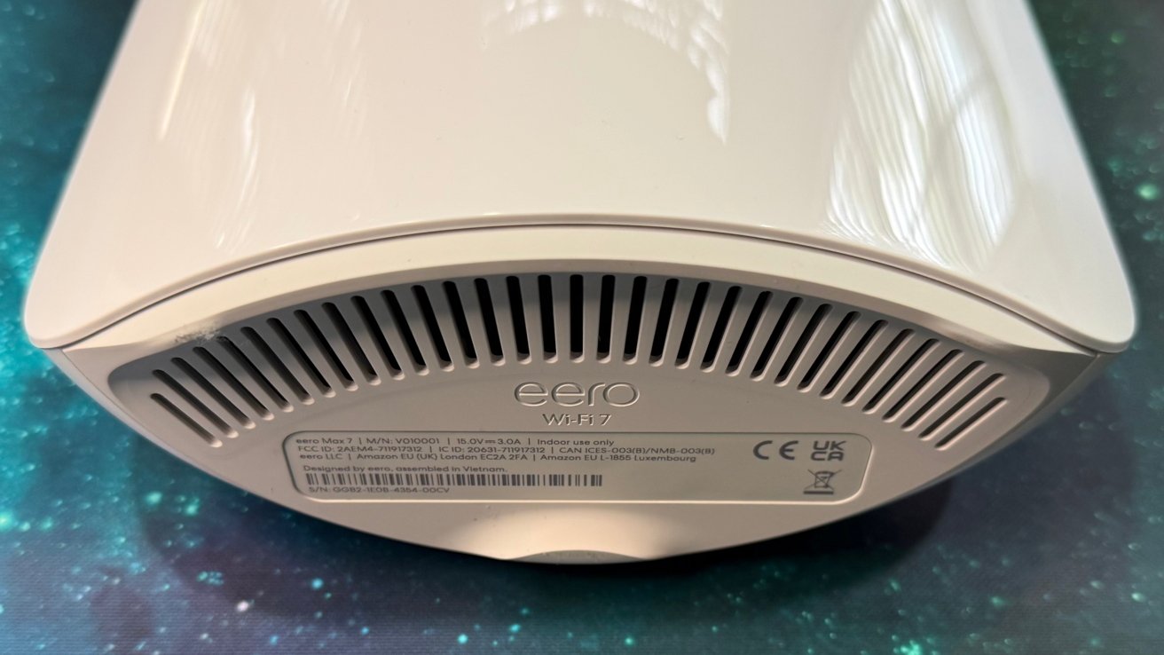 White, oval-shaped electronic device on a galaxy-themed surface, featuring ventilation slits and a label with product information and certifications on the side.