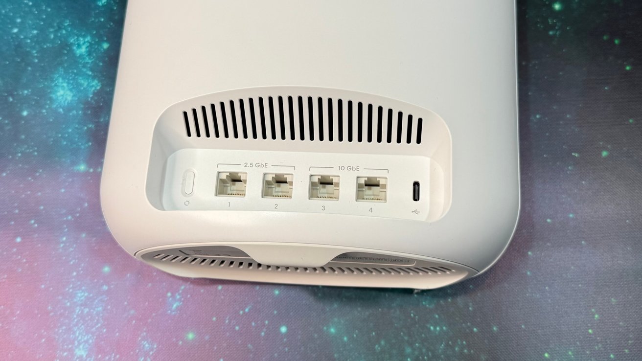 White electronic device with ventilation slots, featuring four Ethernet ports labeled 1 to 4, and a USB-C port on a colorful, starry background.