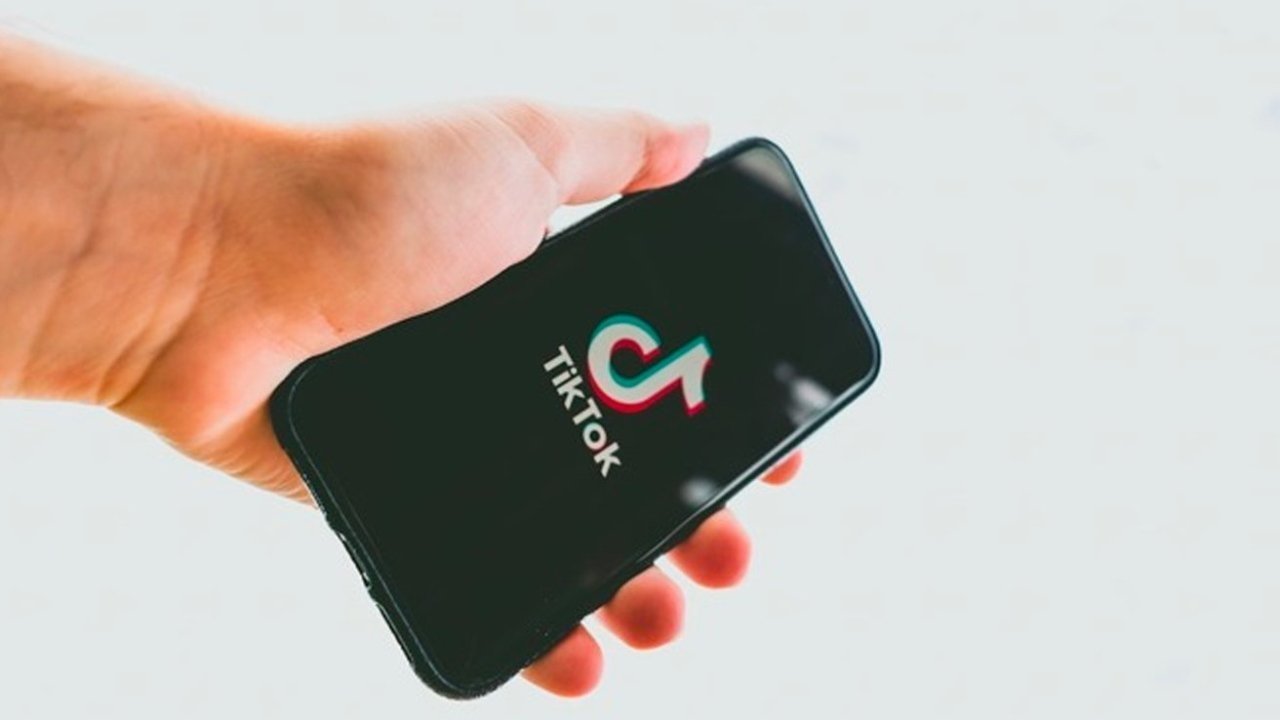 Hand holding a smartphone displaying the TikTok logo on a black screen against a light background.