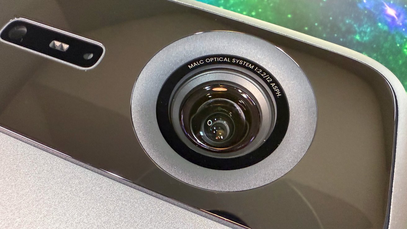 Close-up of a camera lens with the words 'MALC Optical System' on a sleek, metallic surface.
