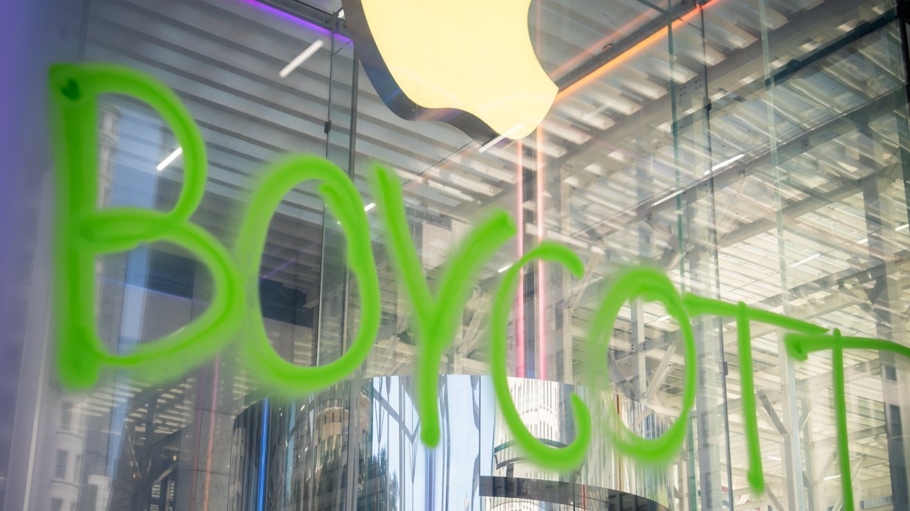 Graffiti spelling 'Boycott' in green paint on a glass surface, with a blurred backdrop of a store interior and an illuminated logo above.