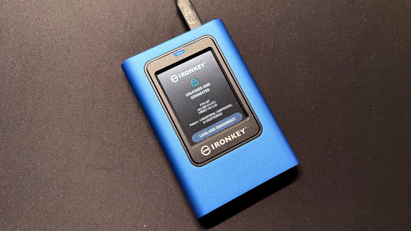 Blue IronKey data device with a screen displaying a lock symbol and status updates. Connected by a cable on a dark surface.