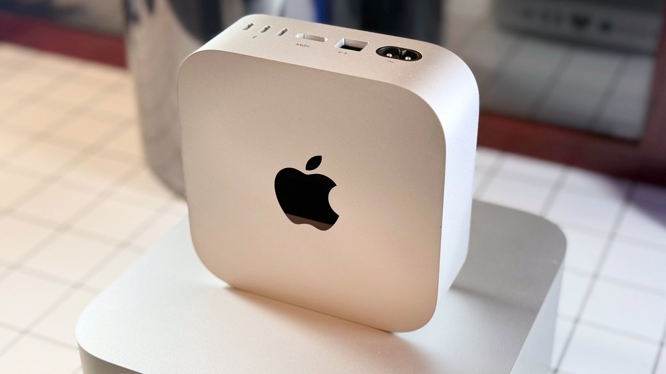Silver compact computer with an Apple logo, placed on a tiled surface. Top features include ports for power, HDMI, and connectivity options.