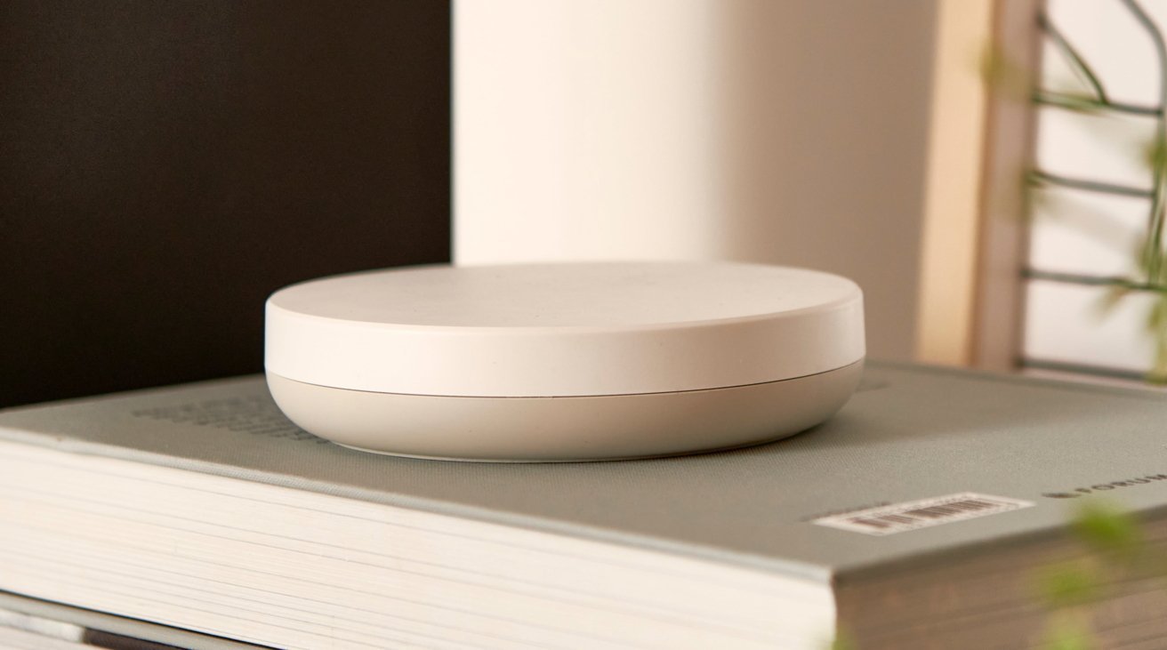 A white, round, flat device sits on top of a closed, hardcover book with a barcode visible.