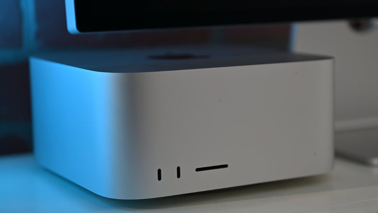 Gray, rectangular computer with rounded edges, small front slots, and a large black screen on top in a softly lit environment.