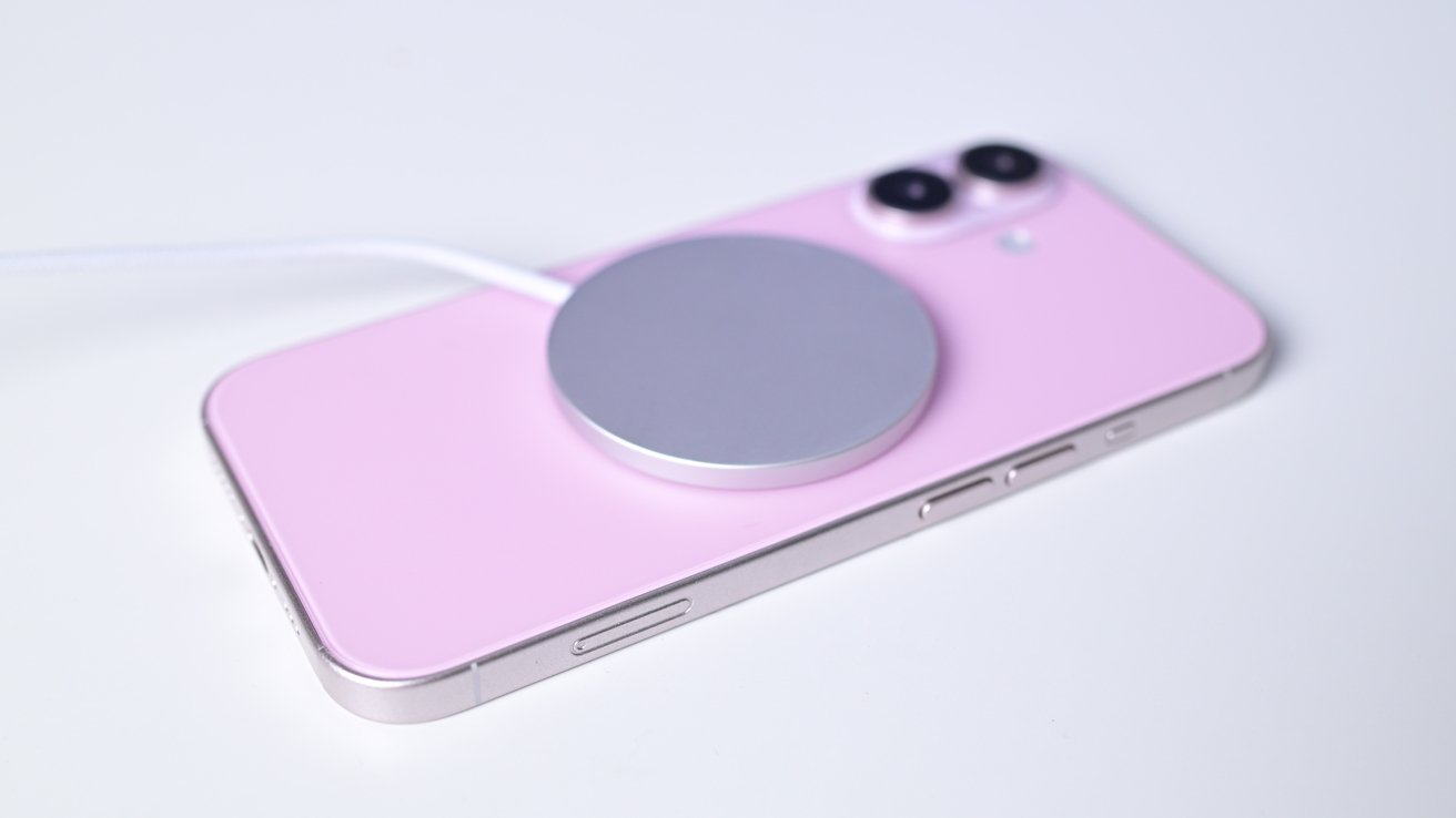 Pink smartphone with dual rear cameras and a circular silver charger attached, set on a white surface.
