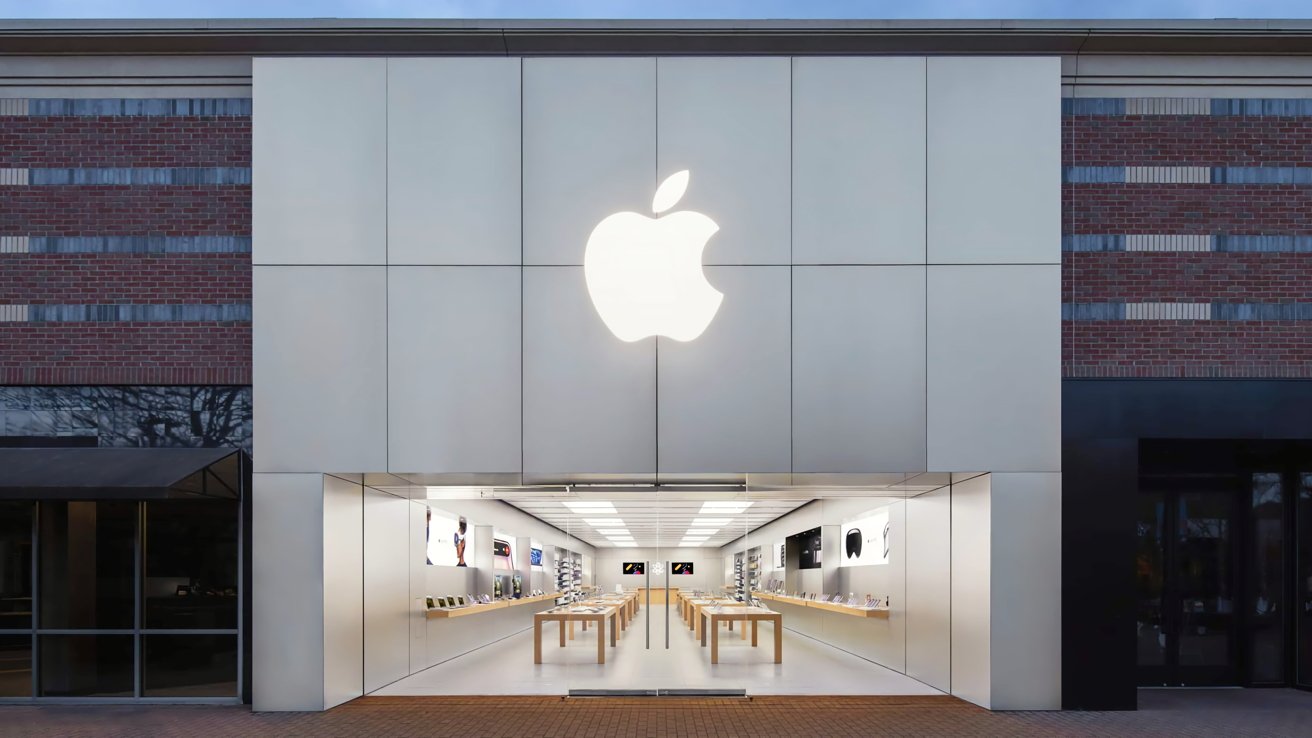 Apple store exterior with a large glowing Apple logo, glass entrance, and interior displaying wooden tables with electronic devices.