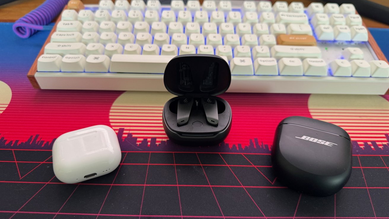 White keyboard and three earbud cases on a vibrant, colorful desk mat showing geometric and skyline patterns.
