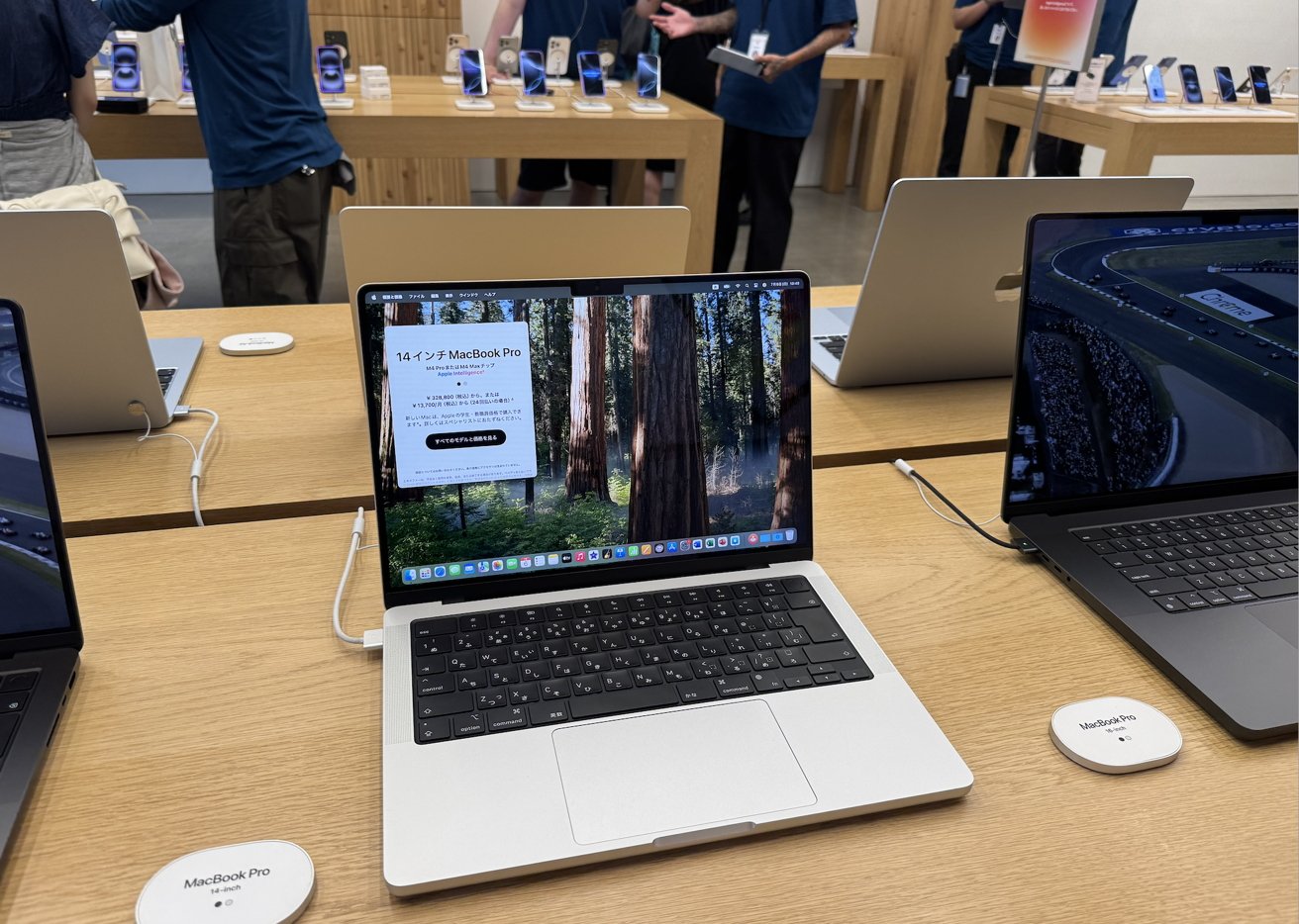 Open laptops on wooden tables in a bright tech store; one displays a race car driver. Staff and devices are visible in the background.