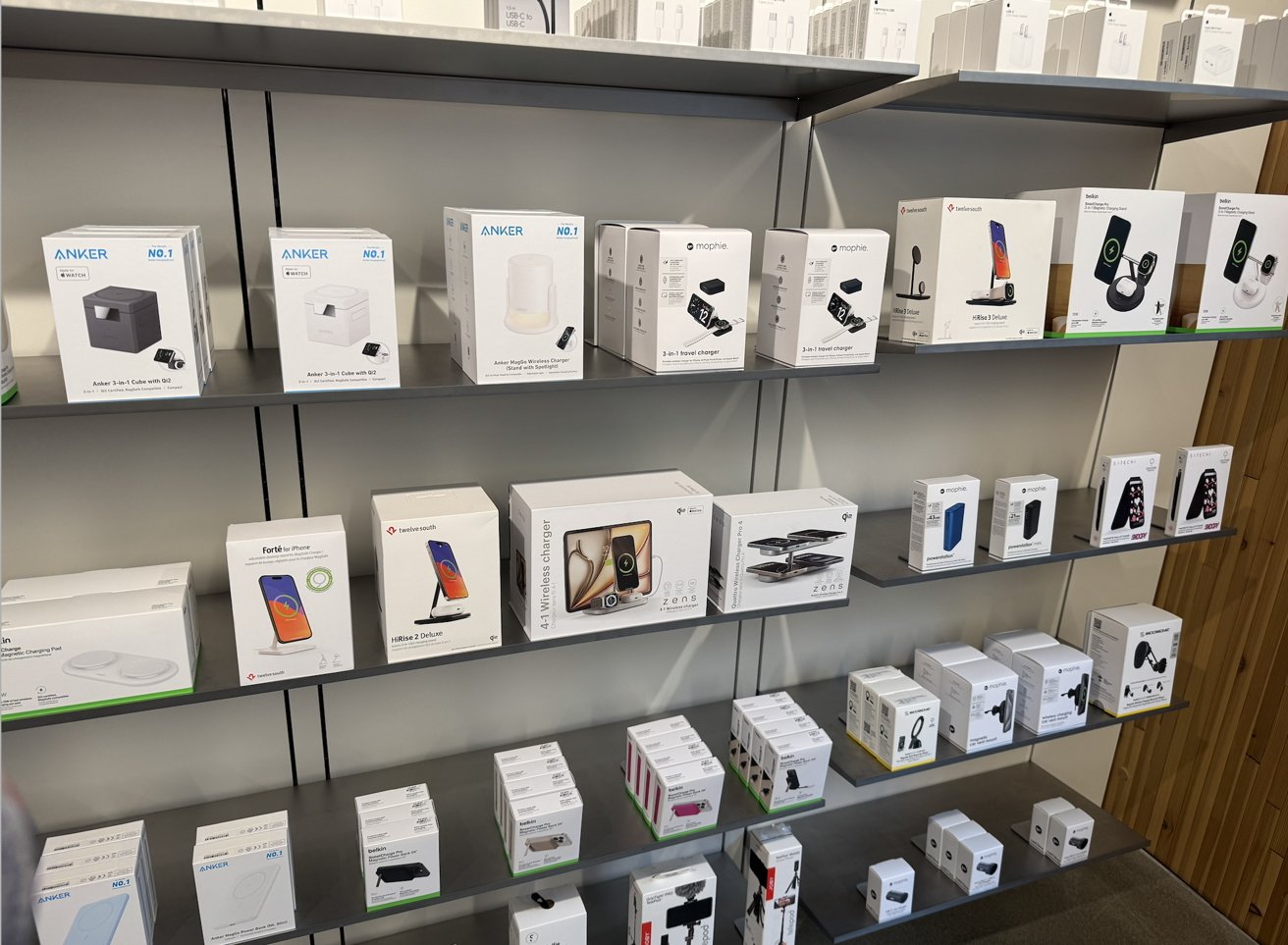 Shelves displaying various electronic device packaging, including chargers, stands, and wireless chargers. Boxes are neatly arranged, showcasing different brands and products in a store setting.