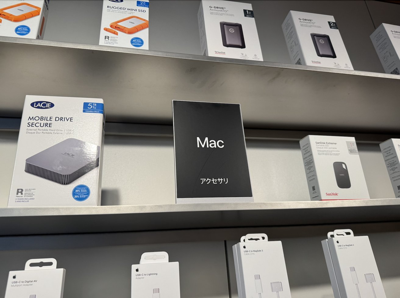 Shelves displaying various hard drives and accessories, with a central sign labeled 'Mac' and Japanese characters.