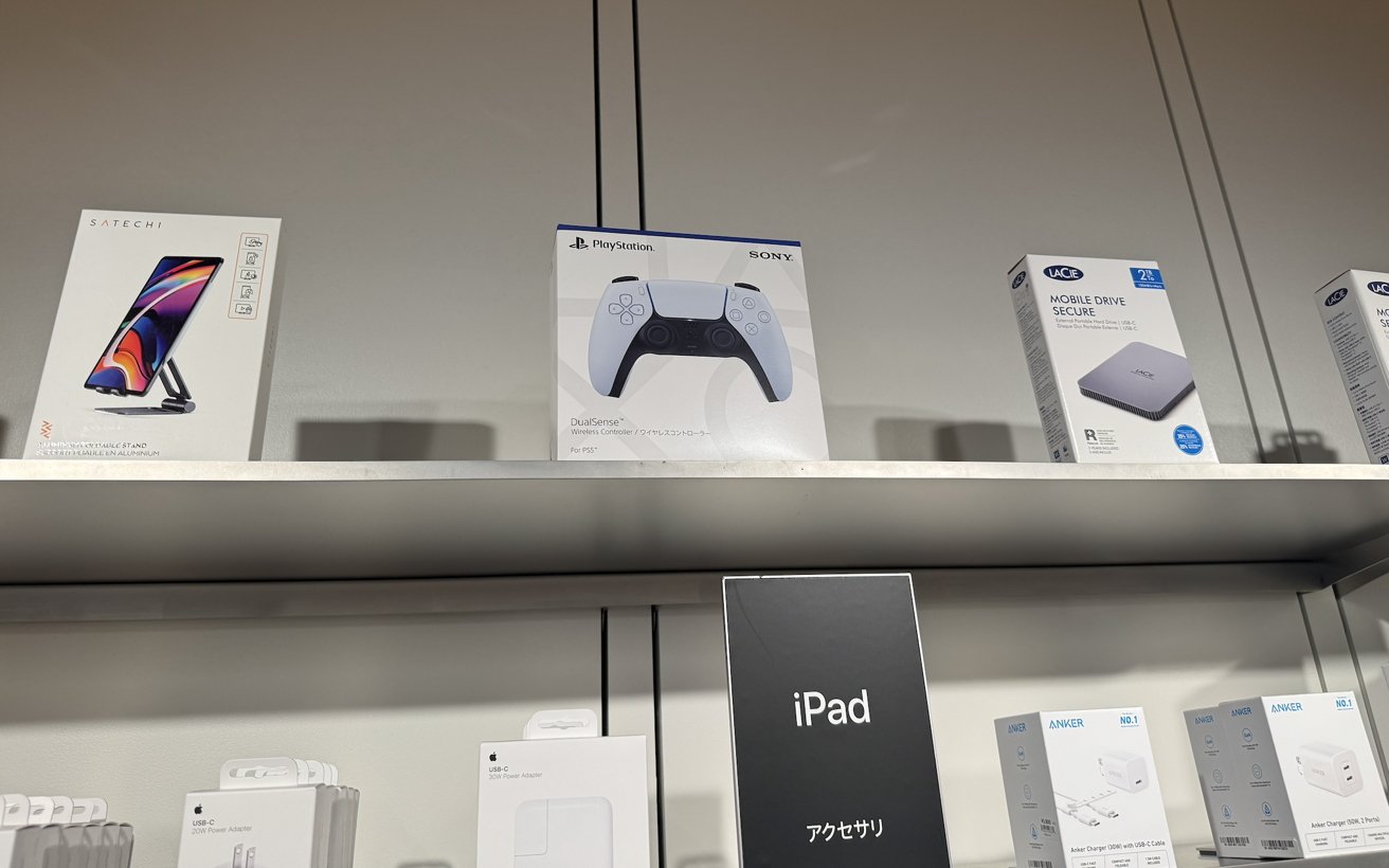 Electronics shelf displaying PlayStation controller, mobile drive, adjustable stand, USB-C power adapters, and iPad accessories in packaging.