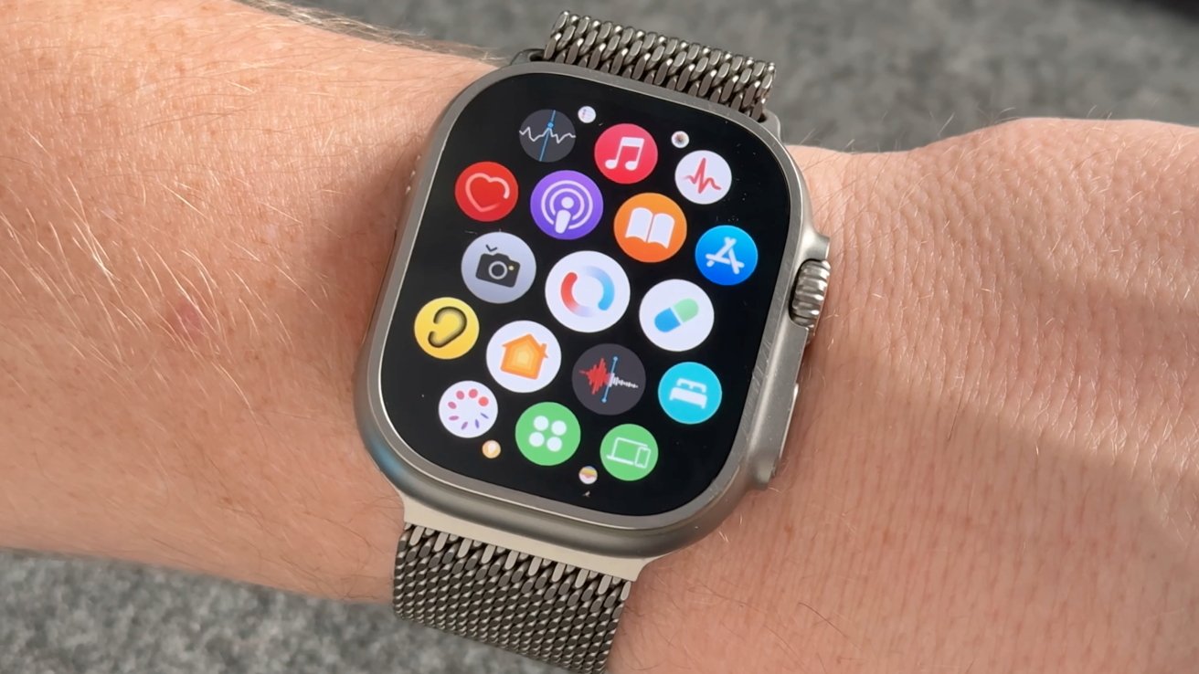 A smartwatch with a metal mesh band displaying app icons on a wrist against a textured background.