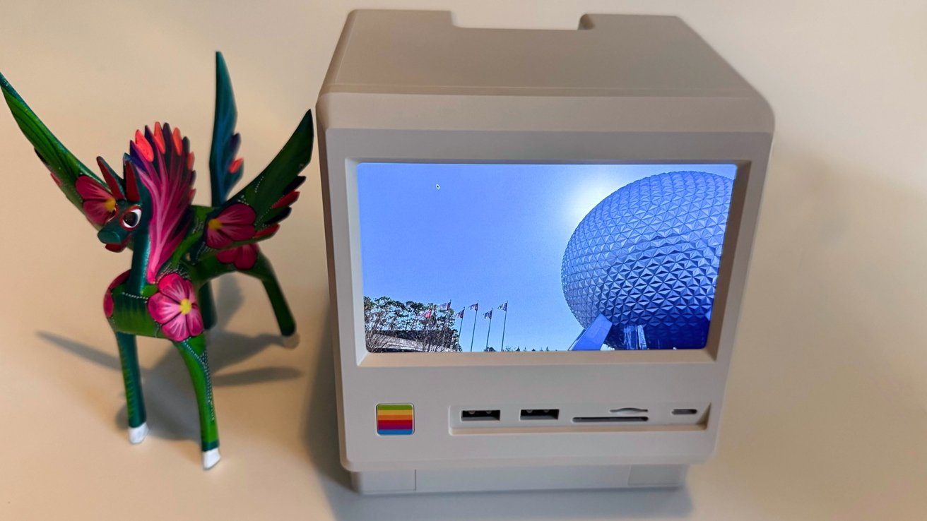 Image: https://photos5.appleinsider.com/gallery/64602-134607-Wokyis-M5-review-3-xl.jpg A small colorful unicorn figurine beside a retro-style computer display showing a geodesic dome against a clear blue sky