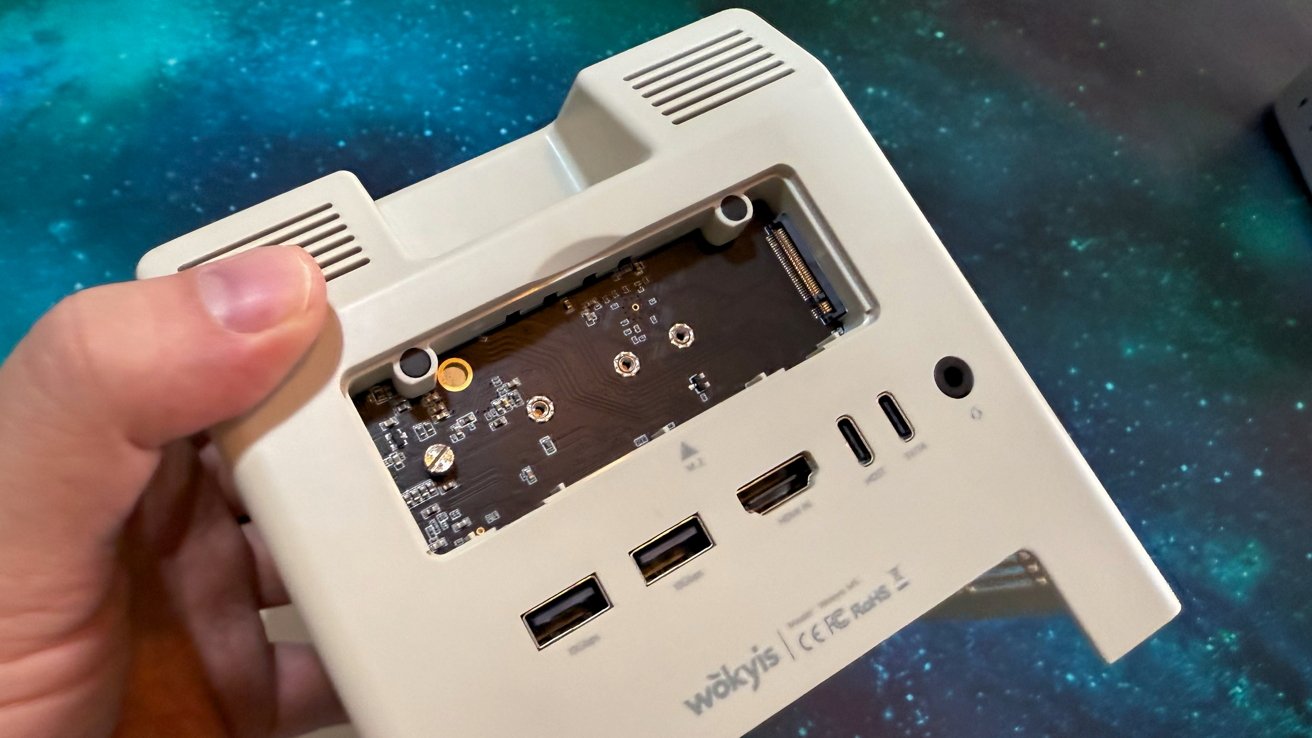 Hand holding a device with exposed circuit board and various ports including USB and HDMI against a starry background