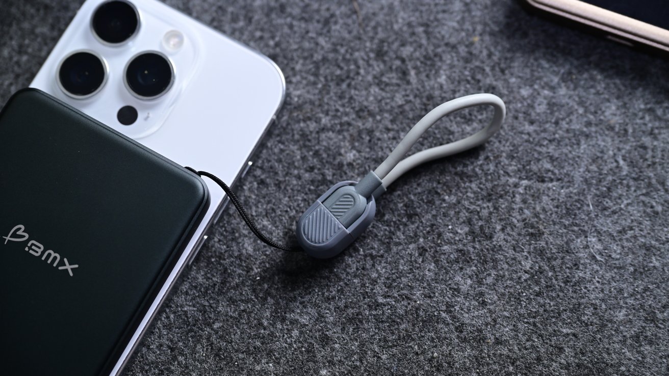 Two smartphones on a gray surface, connected by a small gray and black gadget with a flexible loop.