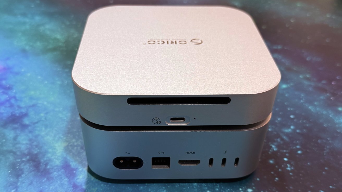 Stacked silver computer components with various ports, including HDMI and USB-C, against a galaxy-themed background.