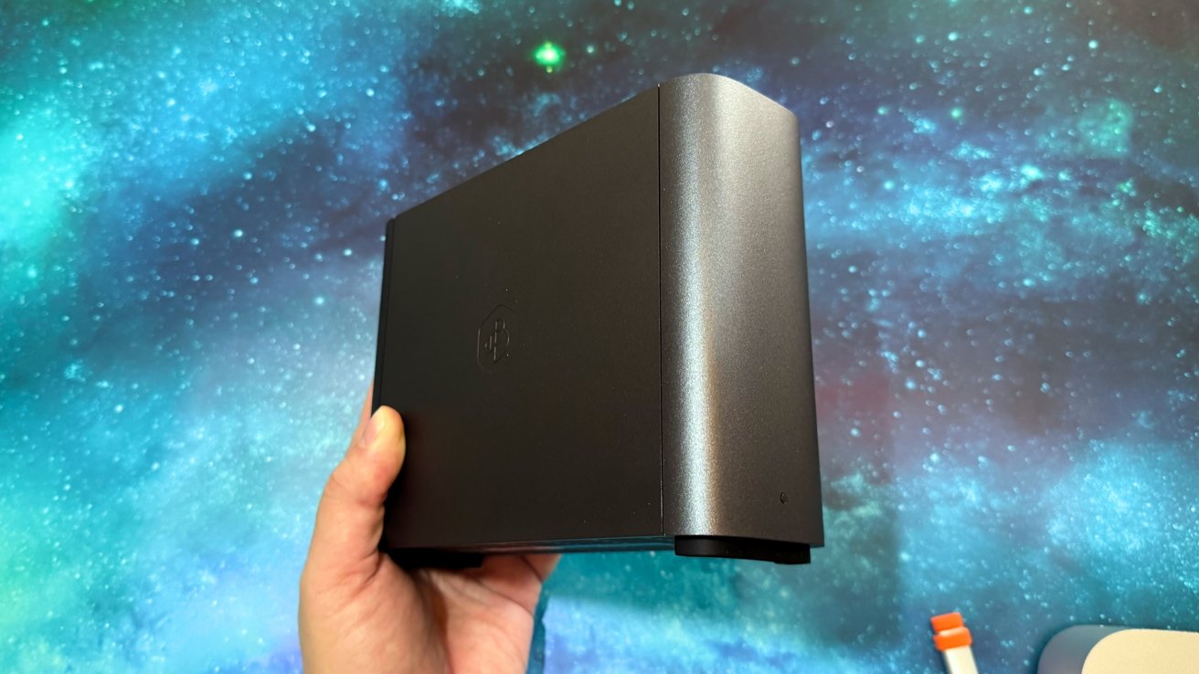 A person holds a black, sleek electronic device against a starry, blue cosmic background.