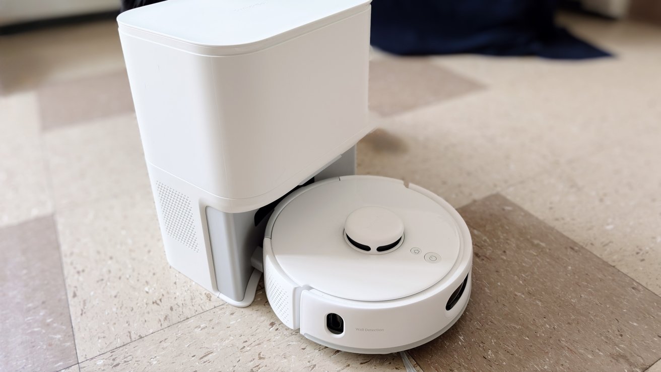 White robotic vacuum with charging station on a beige tiled floor.