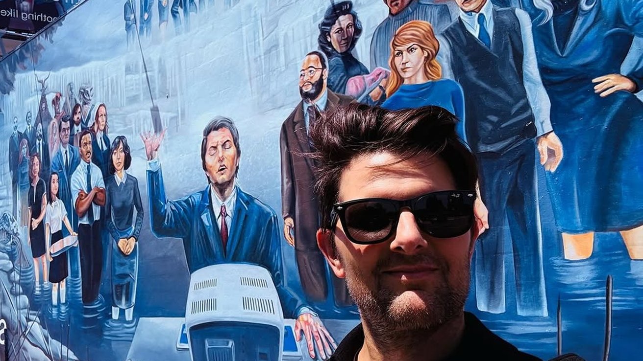 Person wearing sunglasses selfie with a colorful mural depicting a group of diverse, formally dressed people in the background.
