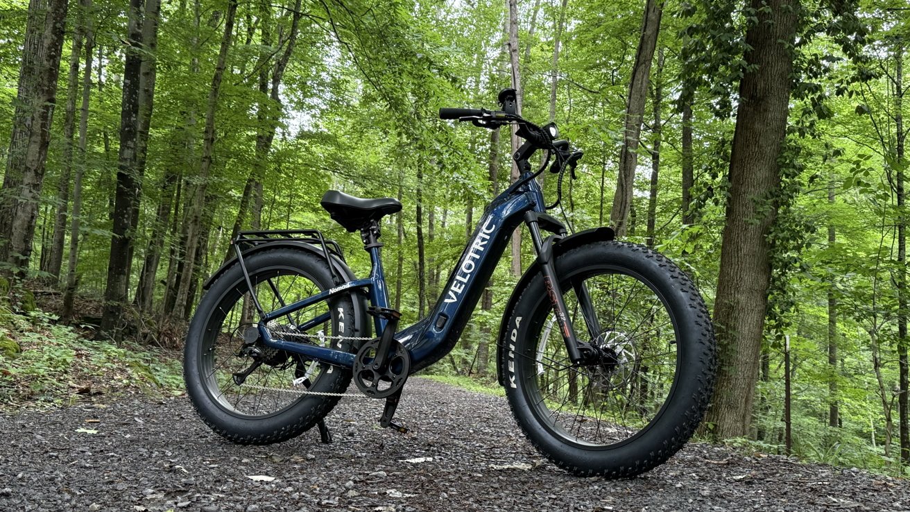 Electric bicycle with thick tires parked on a gravel path in a lush green forest setting.