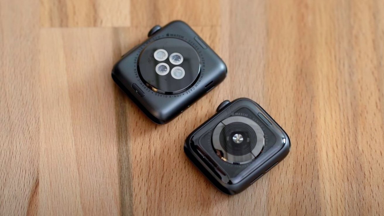 Two black smartwatches face down on a wooden surface, displaying their circular sensors and polished cases.