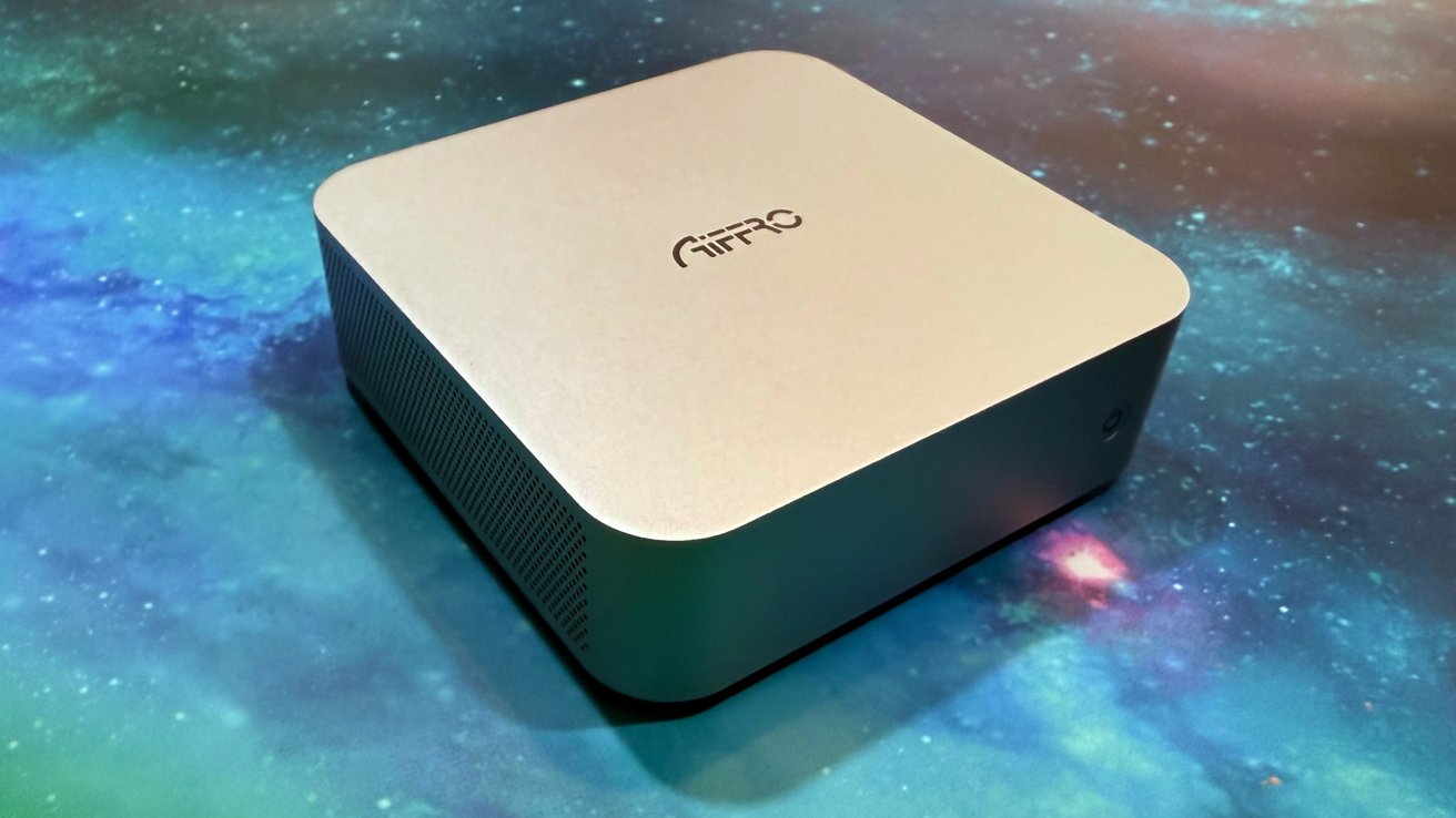 A silver, rectangular electronic device with rounded corners sits on a blue and green galaxy-patterned surface, featuring a circular logo on top.