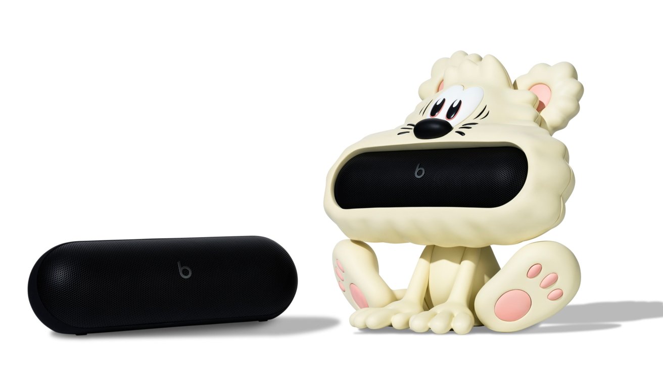 Black speaker beside a whimsical character speaker holder with a large mouth, cartoon eyes, and pink paw-like feet on a white background.
