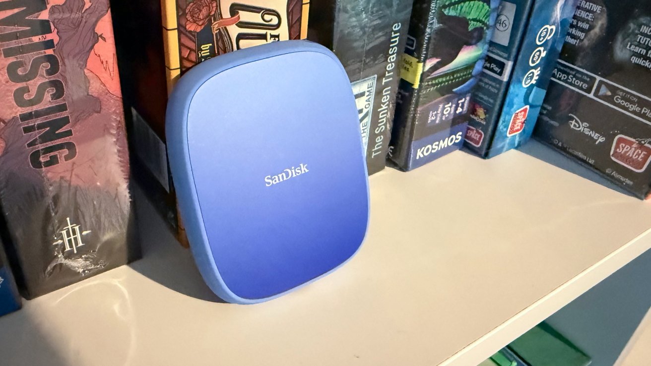 Blue SanDisk external hard drive on a white shelf, surrounded by colorful board game boxes.