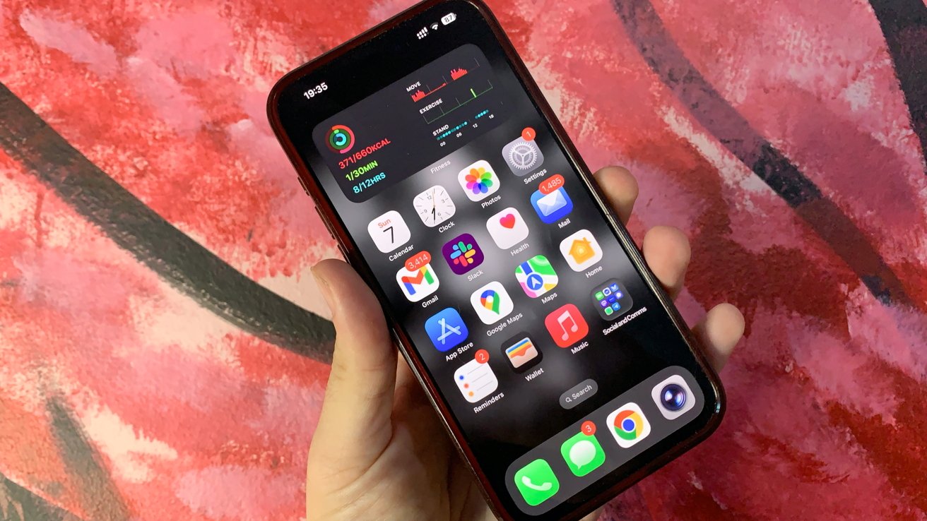 Hand holding a smartphone displaying various app icons on the screen, with a red and pink textured background.