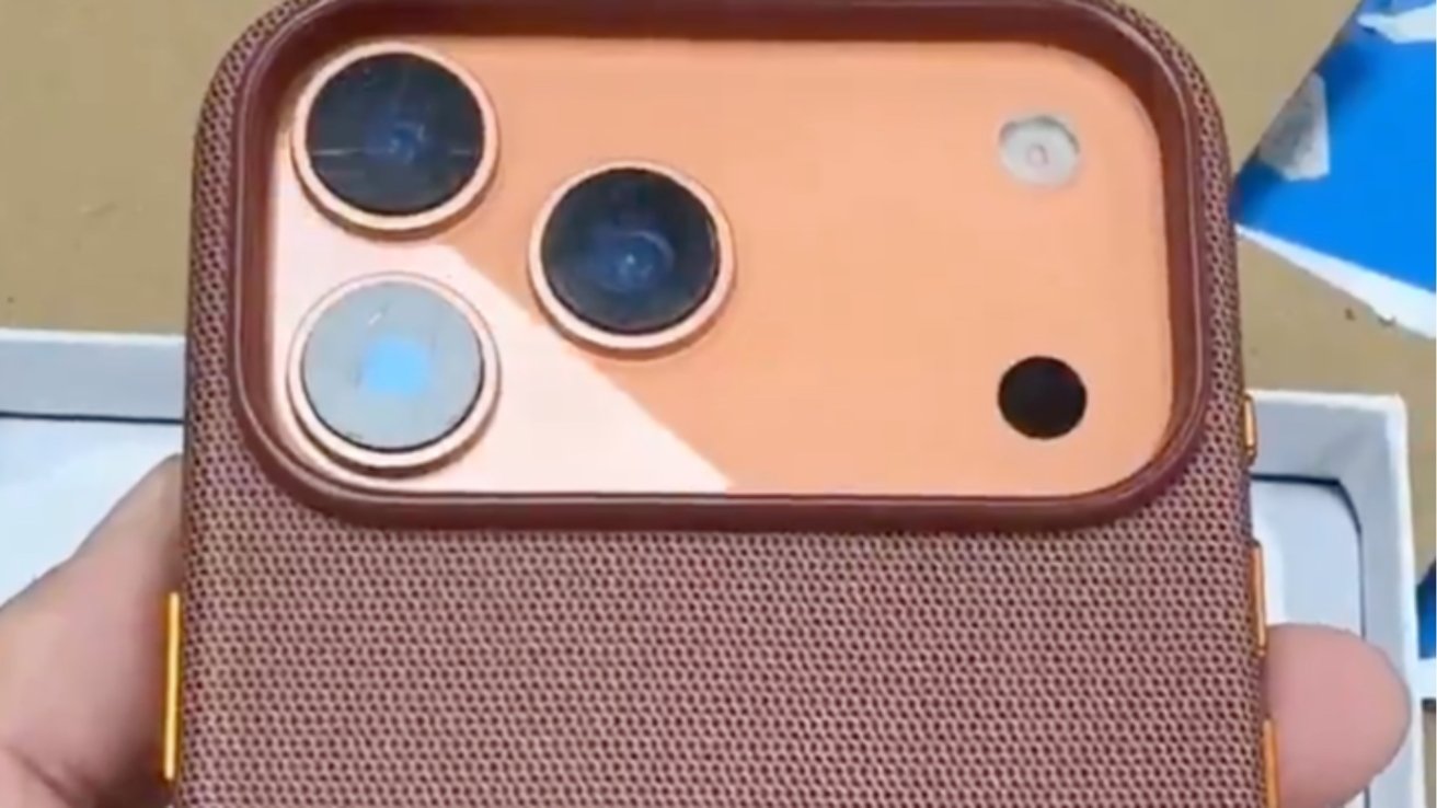 Brown textured phone case with three circular camera lenses on a peach-colored background, held in a person's hand.