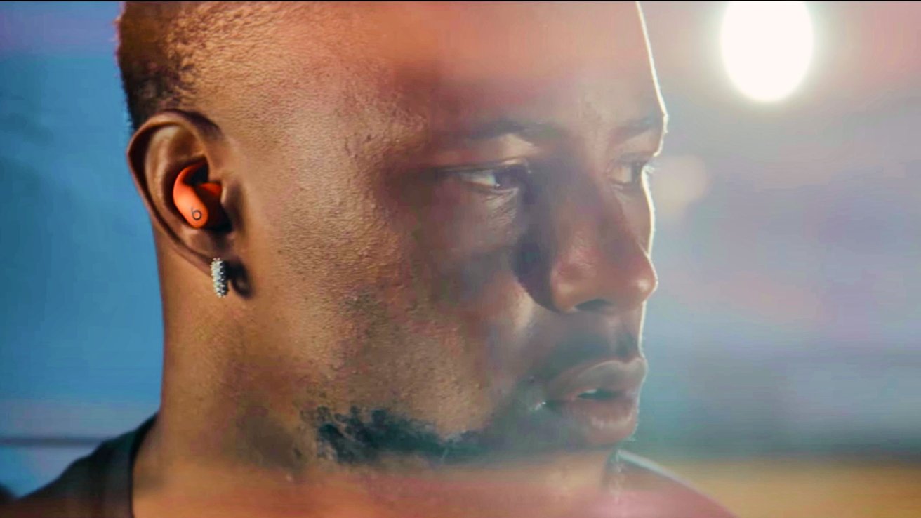 Person wearing orange earbuds and a diamond earring, looking to the side, with a blurred bright background.