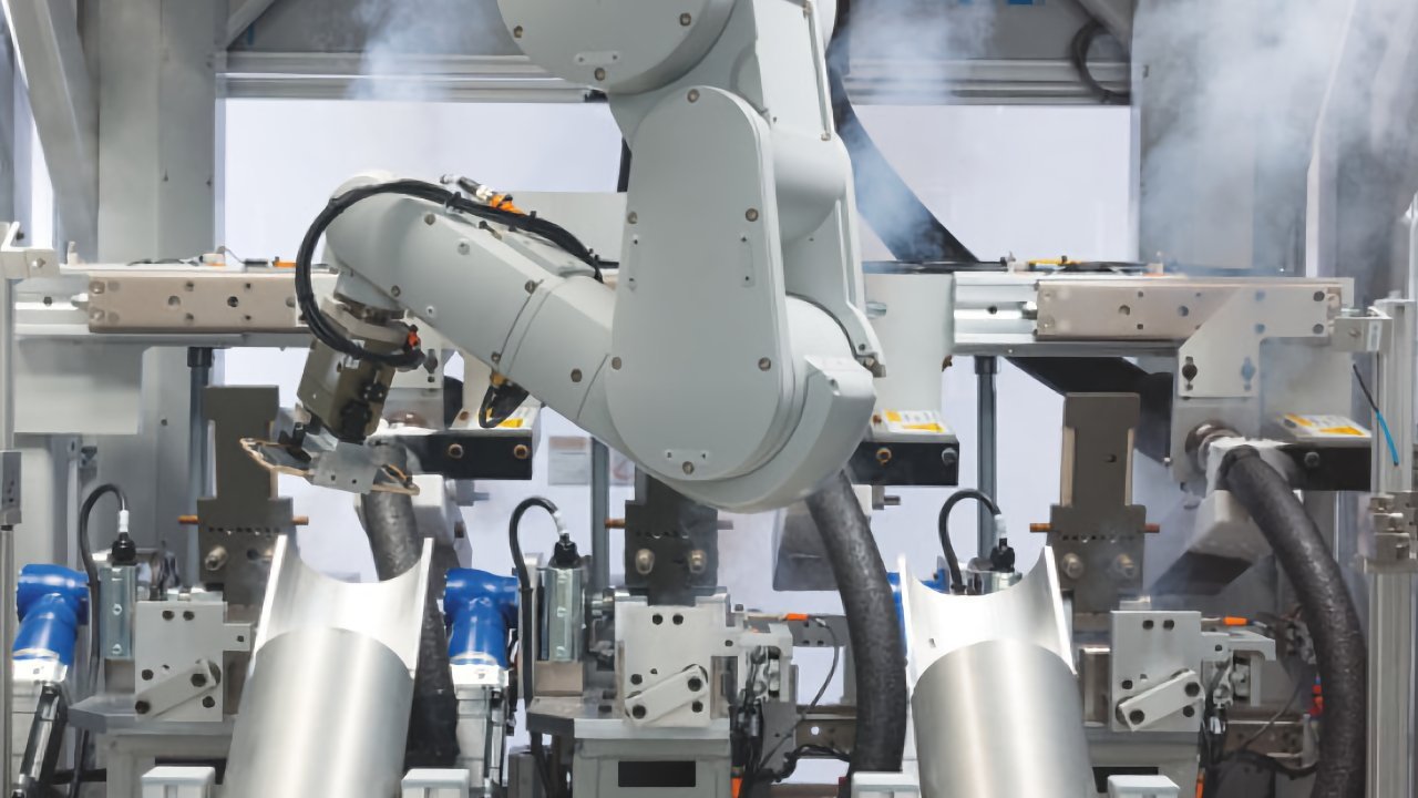 Robotic arm in a factory setting, with machinery components and large metal pipes, surrounded by light smoke.