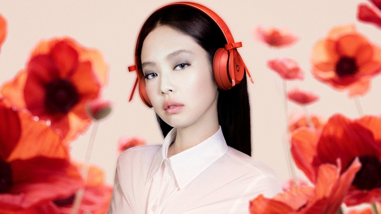 Person wearing red headphones with red poppy flowers in the foreground, dressed in a white shirt against a soft pink background.