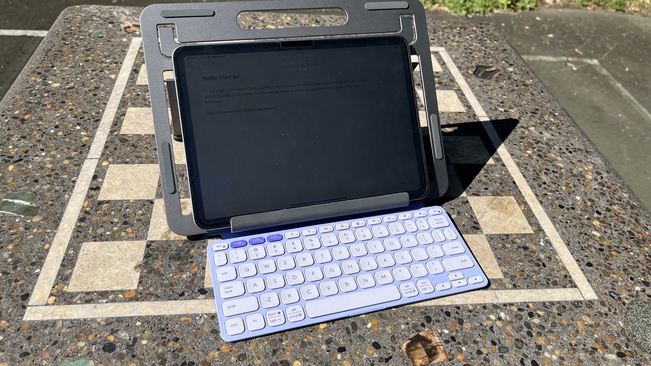 Tablet on a stand with wireless keyboard on a stone chessboard table, outdoors in daylight.