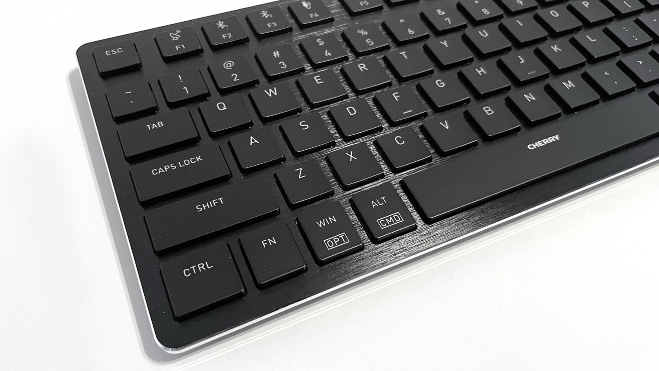 Black computer keyboard with white lettering on keys, labeled ESC, F1-F12, TAB, CAPS LOCK, SHIFT, CTRL, ALT, CMD, and WIN. Brand name Cherry visible.