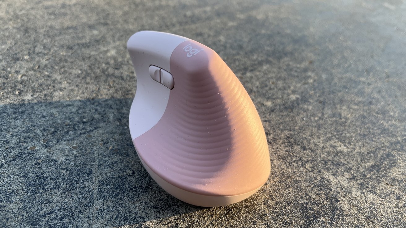 Ergonomic pink vertical computer mouse lying on a textured gray surface, featuring a scroll wheel and a gentle curve design.
