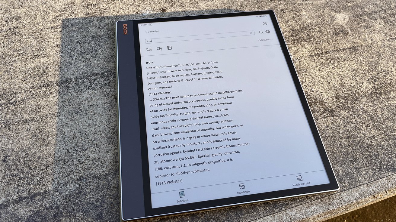 A digital e-reader on a stone surface displays a dictionary entry for 'iron,' detailing its definition and chemical properties.