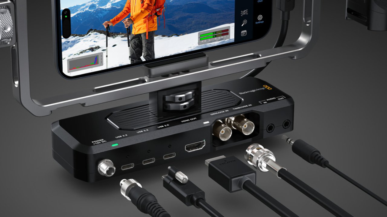 Video capture device with multiple cable connections, a smartphone displaying mountains and a person in orange jacket on screen, surrounded by various input and output ports.