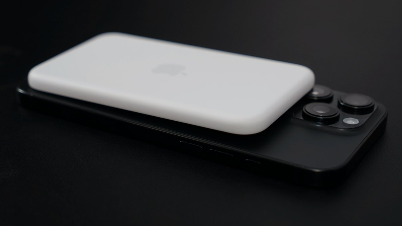 A white wireless charging pack placed on top of a black smartphone with triple rear cameras on a dark surface.