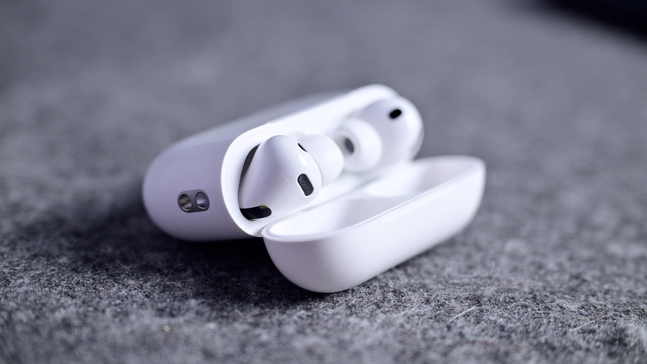 White wireless earbuds in an open charging case on a gray textured surface.