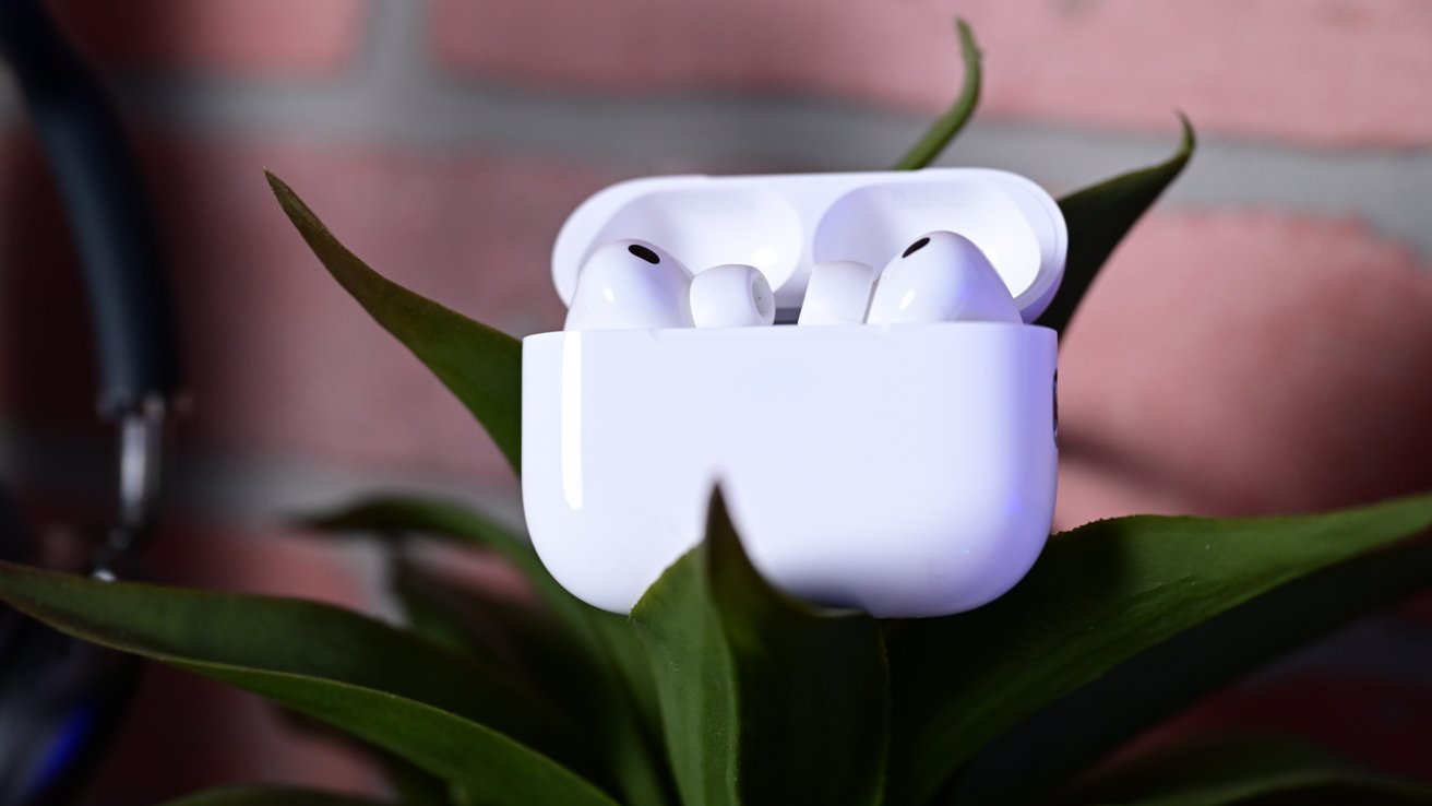White wireless ears in an open charging case, resting on green leaves with a blurry background of the wall wall.