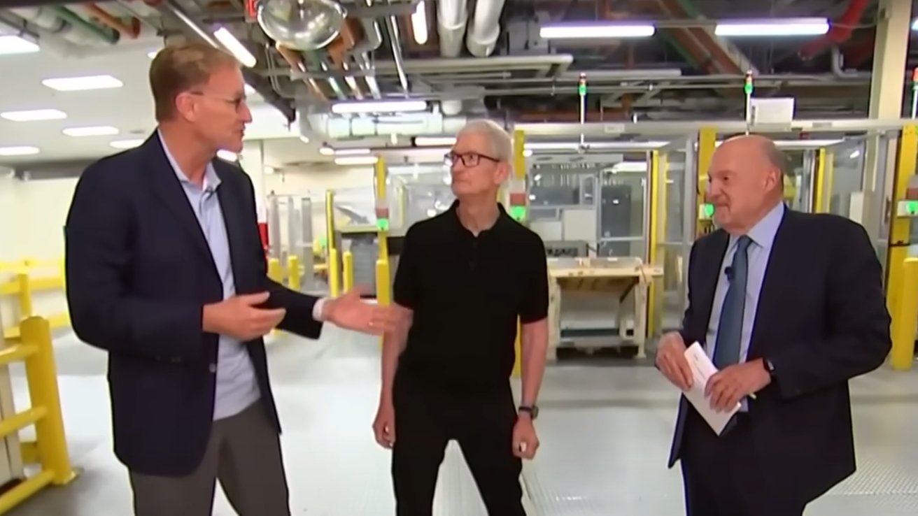 Three men stand inside a modern industrial facility, with one gesturing while others listen. They are surrounded by equipment and bright lights.