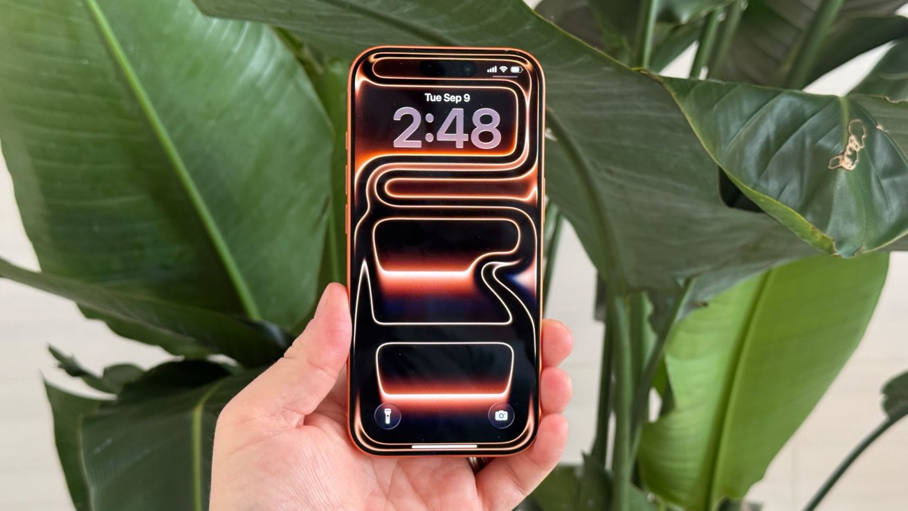 Hand holding a smartphone with vibrant abstract wallpaper and 2:48 time display, near large green leaves in the background.