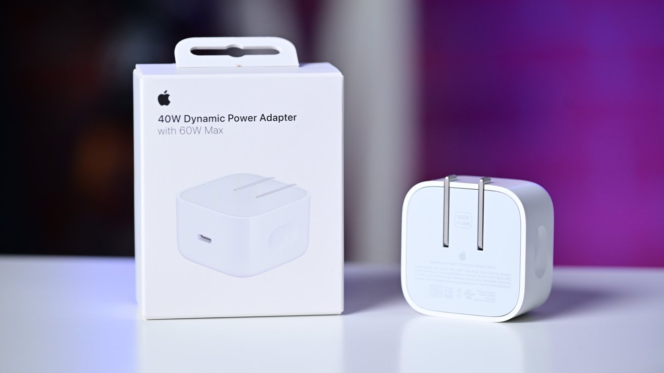 White 40W dynamic power adapter and its box on a reflective surface with a blurred purple background.