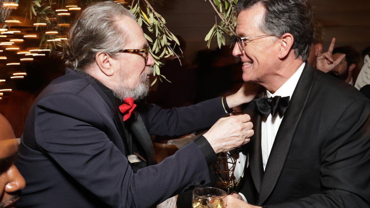 Two men in formal attire share a joyful moment at a party, surrounded by warm lighting and greenery.